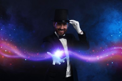 Smiling magician showing trick on dark background