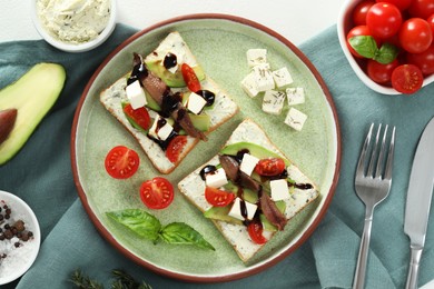 Delicious sandwiches with anchovies, cheese and tomato served on white table, flat lay