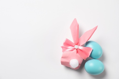 Photo of Easter bunny gift bag and dyed eggs on white background, top view