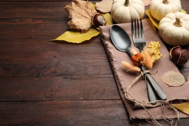 Seasonal table setting, space for text. Cutlery with pumpkins and autumn leaves on wooden background