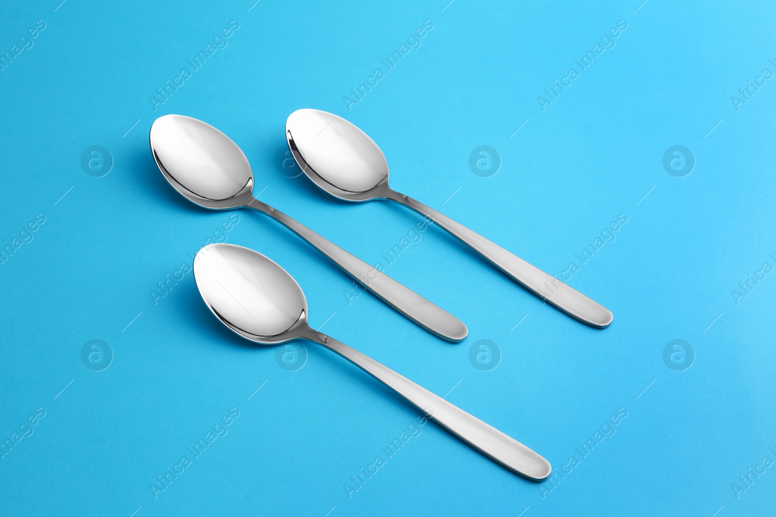 Photo of Clean empty table spoons on blue background