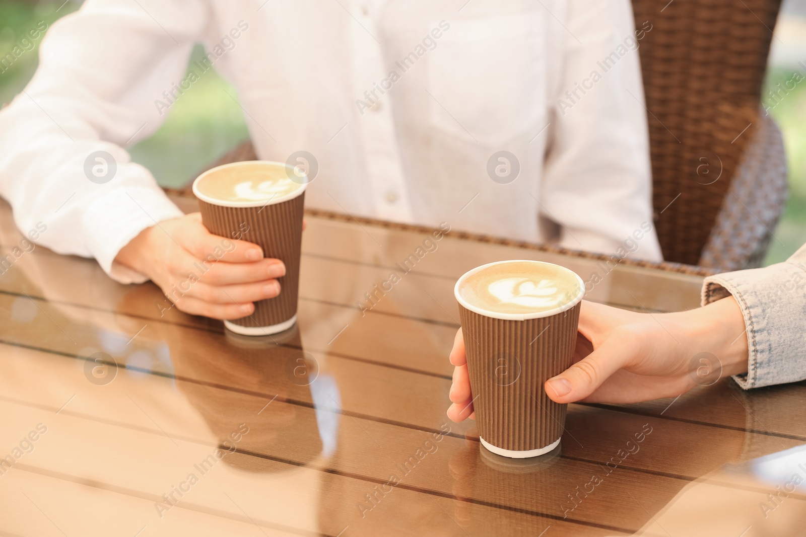 Photo of Women holding takeaway paper cups at table, closeup. Coffee to go