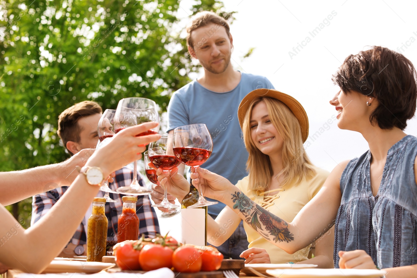 Photo of Young people with glasses of wine at table outdoors. Summer barbecue