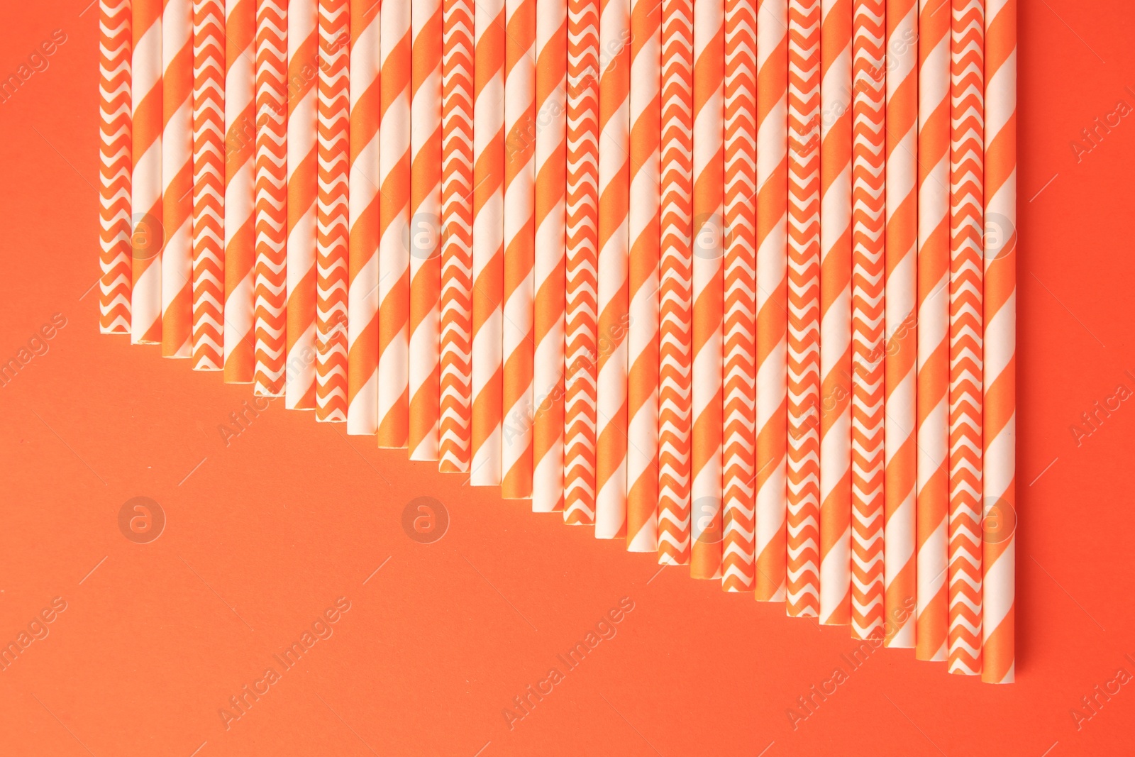Photo of Many striped paper drinking straws on orange background, flat lay