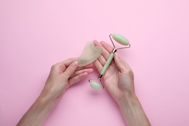 Woman holding gua sha tool and face roller on pink background, top view