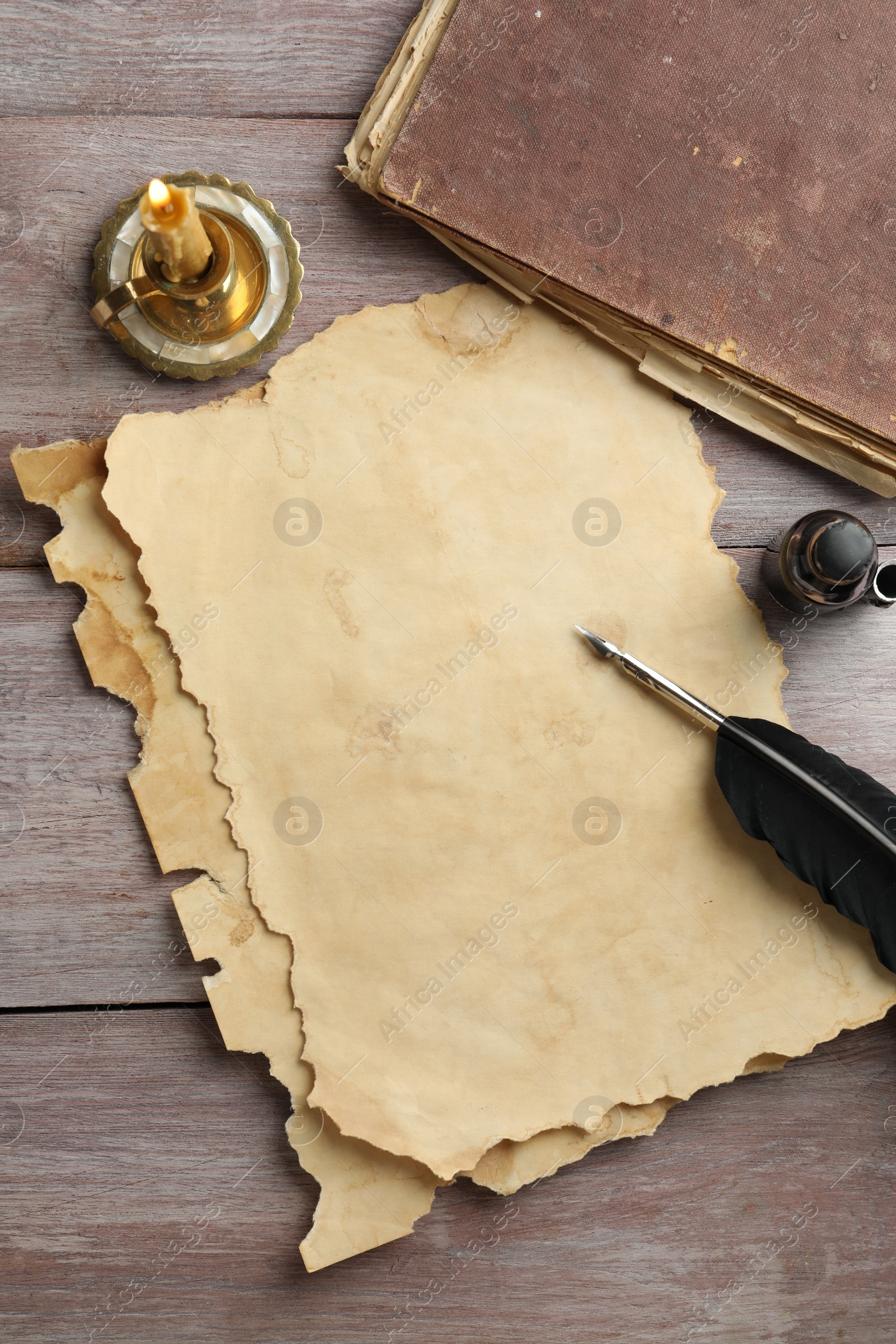 Photo of Sheet of old parchment paper, black feather, inkwell, vintage book and candle on wooden table, flat lay