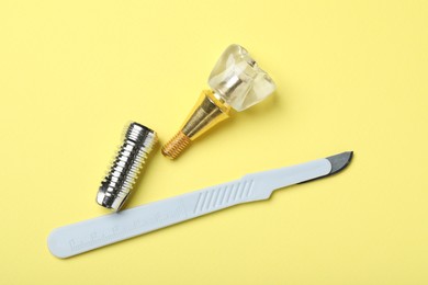 Photo of Parts of dental implant and medical knife on yellow background, flat lay