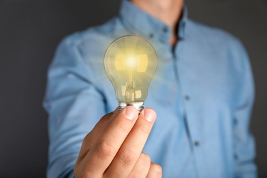 Image of Man holding glowing light bulb on grey background, closeup
