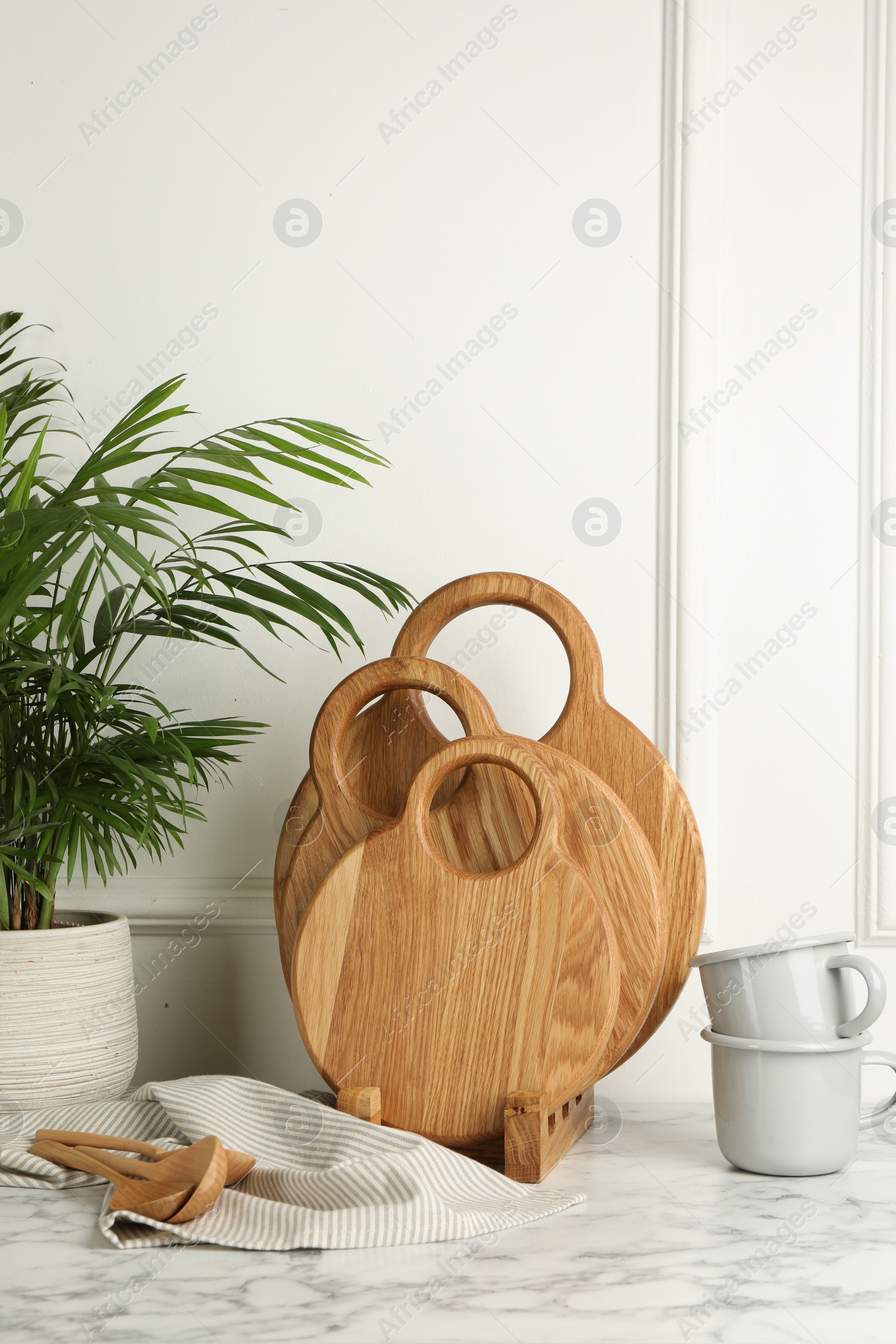 Photo of Wooden cutting boards, spoons, dishware and houseplant on white marble table