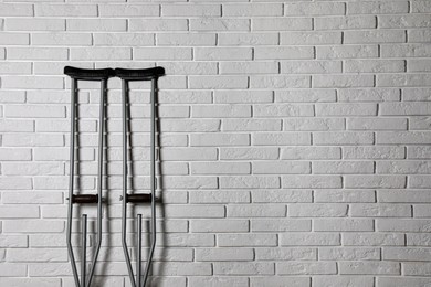 Photo of Pair of axillary crutches near white brick wall. Space for text