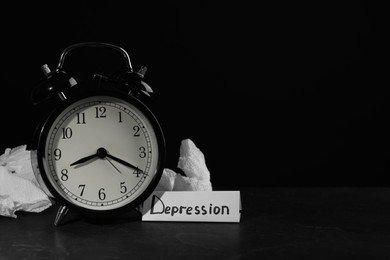 Photo of Depression sign, alarm clock and used tissues on black table against dark background, space for text