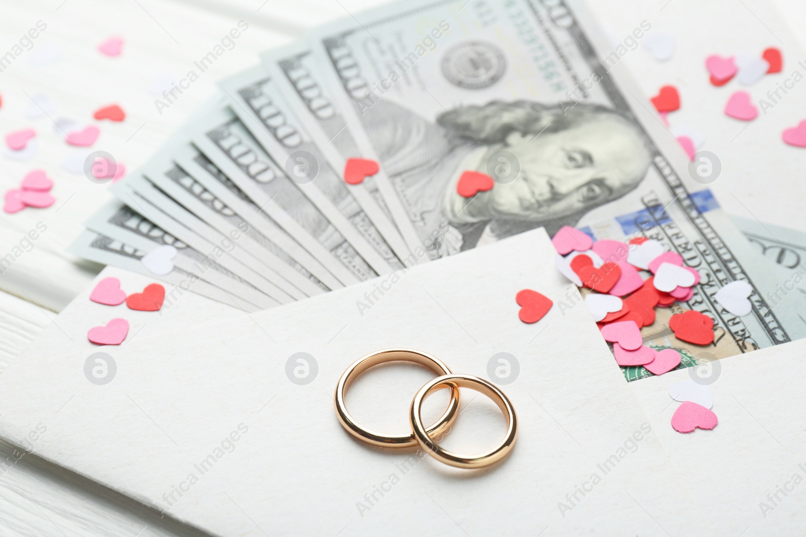 Photo of Honeymoon concept. Two golden rings, money and cutout hearts on white wooden table, closeup