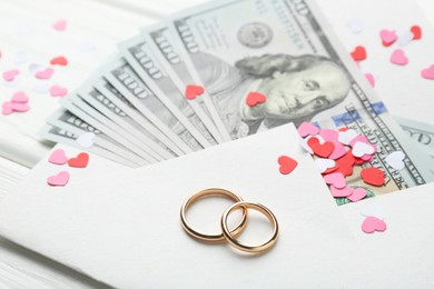 Honeymoon concept. Two golden rings, money and cutout hearts on white wooden table, closeup