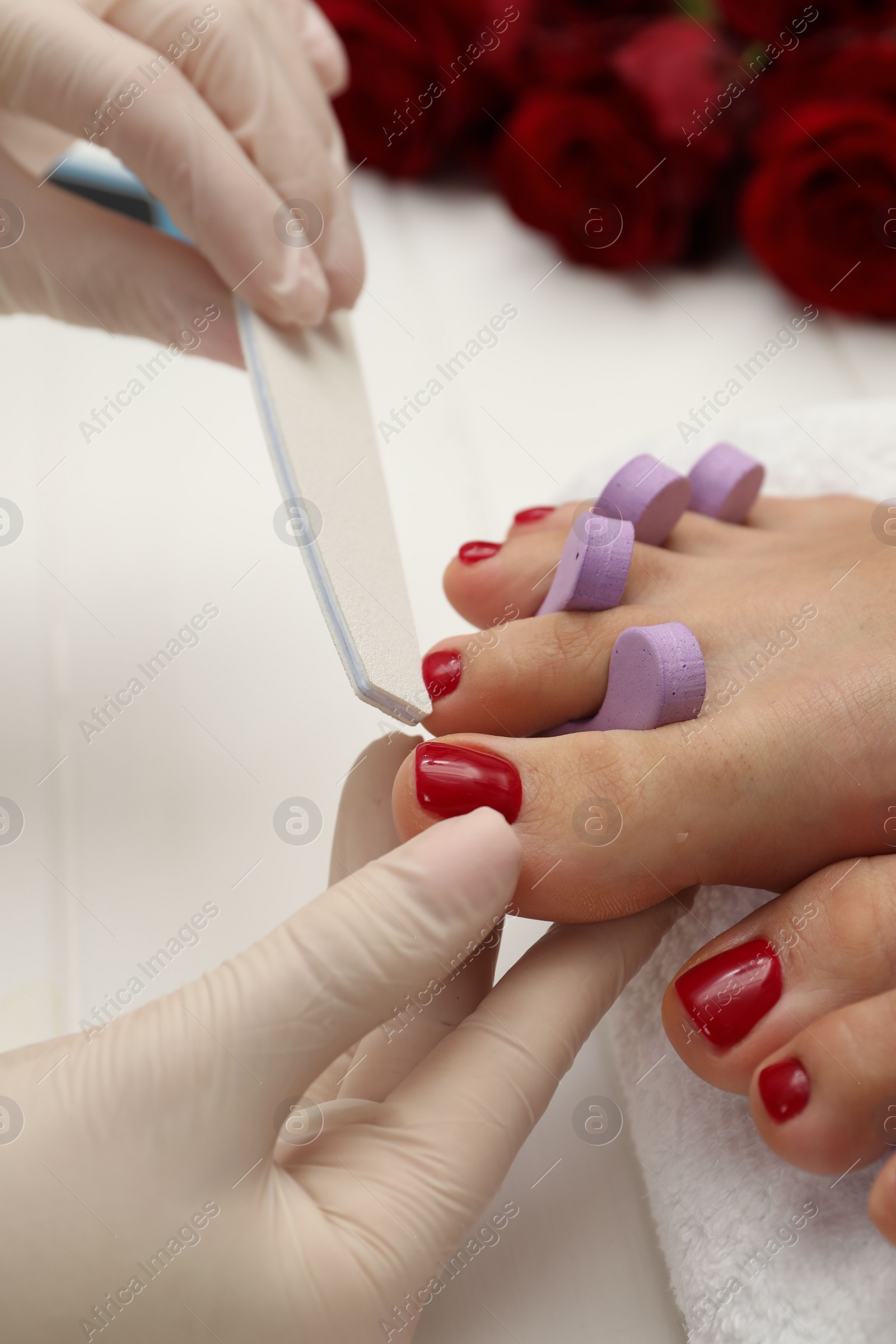 Photo of Pedicurist filing client`s toenails in beauty salon, closeup