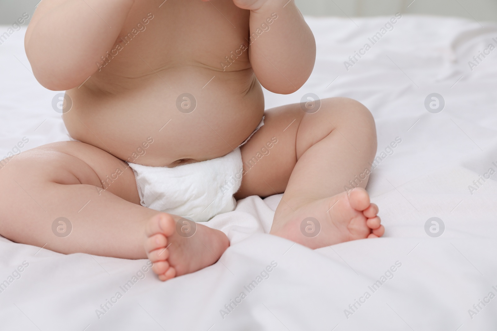 Photo of Cute baby in diaper sitting on bed, closeup