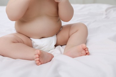 Cute baby in diaper sitting on bed, closeup