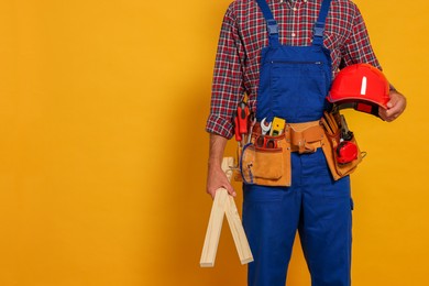 Professional builder in uniform with wooden bars and tool belt on yellow background, closeup. Space for text
