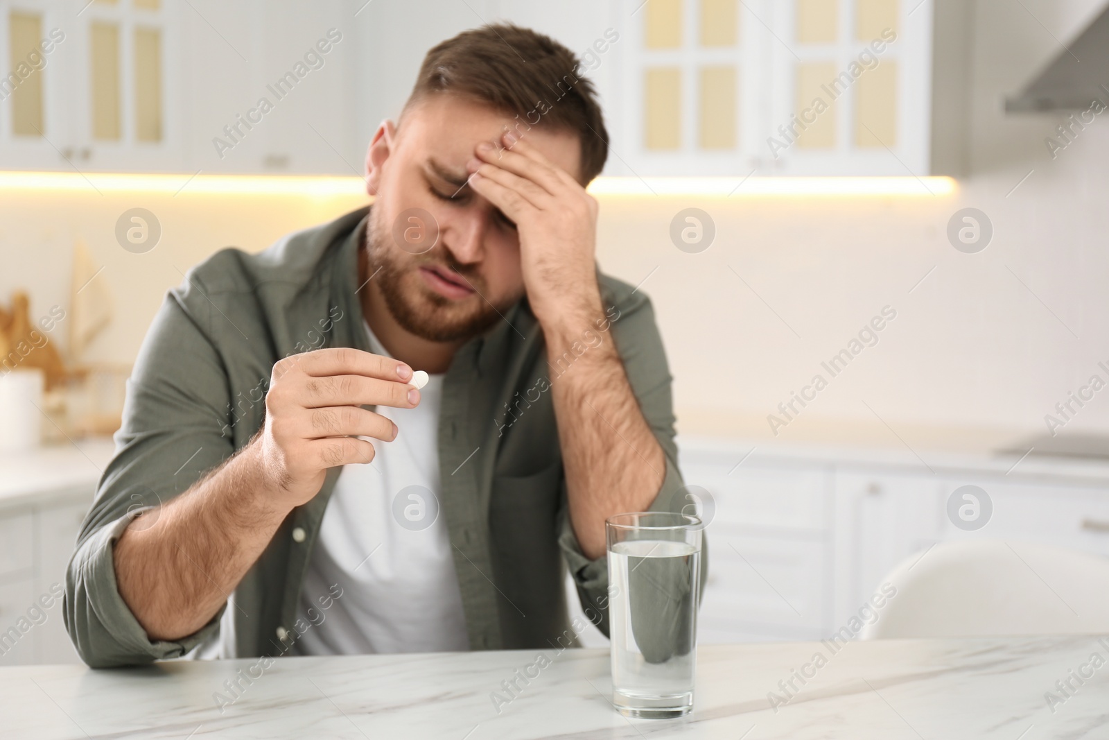 Photo of Man with pill suffering from migraine in kitchen, focus on hand. Space for text