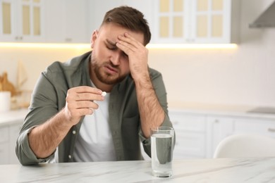 Man with pill suffering from migraine in kitchen, focus on hand. Space for text