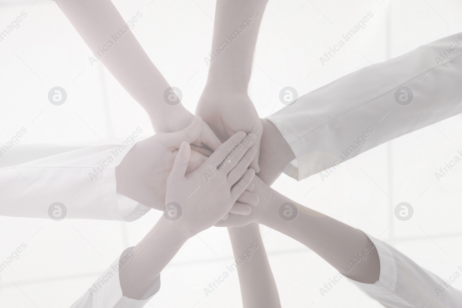 Image of Team of medical workers holding hands together on light background, bottom view. Unity concept