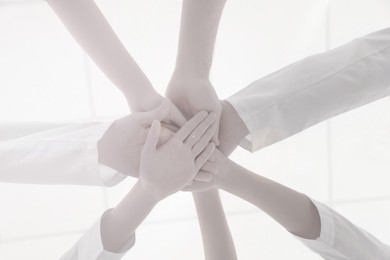 Team of medical workers holding hands together on light background, bottom view. Unity concept