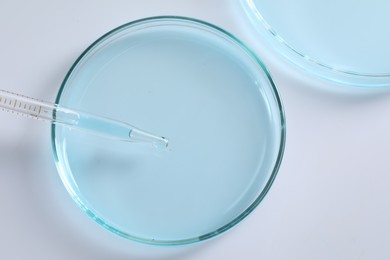 Photo of Dripping liquid from pipette into petri dish at white background, top view. Laboratory analysis