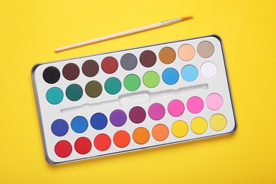 Watercolor palette and brush on yellow background, flat lay
