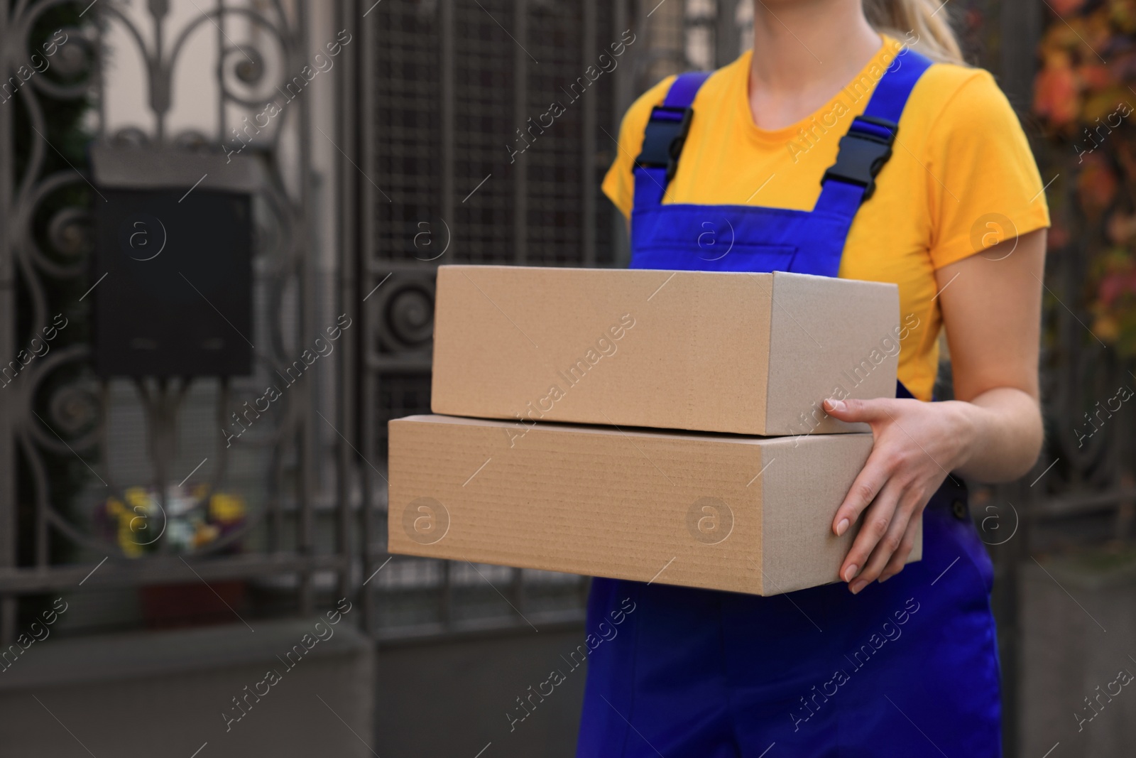Photo of Courier in uniform with parcels near private house outdoors, closeup