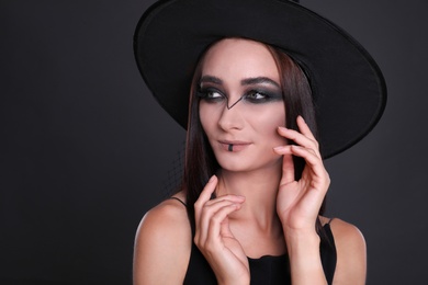 Photo of Mysterious witch wearing hat on black background, closeup