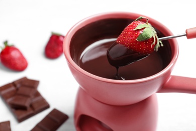 Photo of Dipping strawberry into pot with chocolate fondue on table, closeup