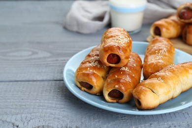 Delicious sausage rolls and milk on grey wooden table, closeup. Space for text