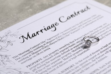 Marriage contract and ring with gemstone on grey table, closeup