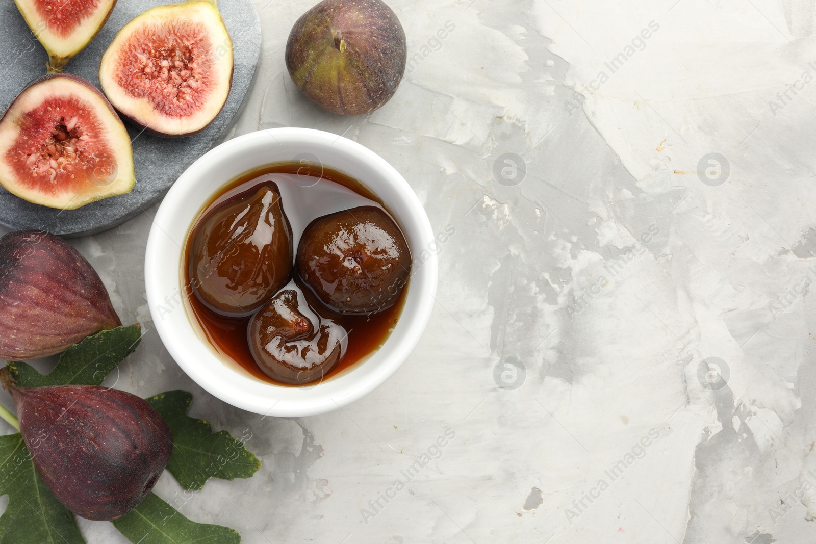 Photo of Bowl of tasty sweet jam and fresh figs on grey table, flat lay. Space for text