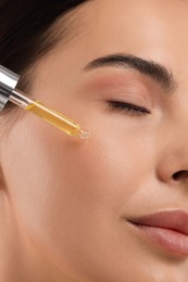 Beautiful young woman applying serum onto her face, closeup