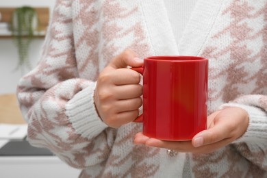 Photo of Woman holding red mug at home, closeup. Mockup for design