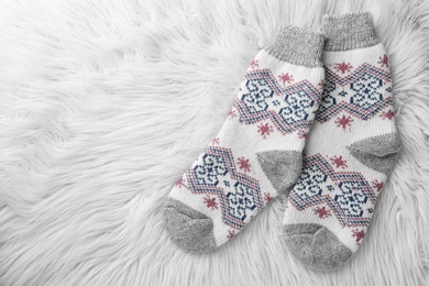 Photo of Knitted socks on white faux fur, flat lay. Space for text
