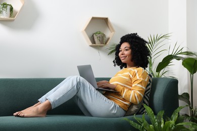 Photo of Relaxing atmosphere. Happy woman with laptop on sofa near houseplants in room