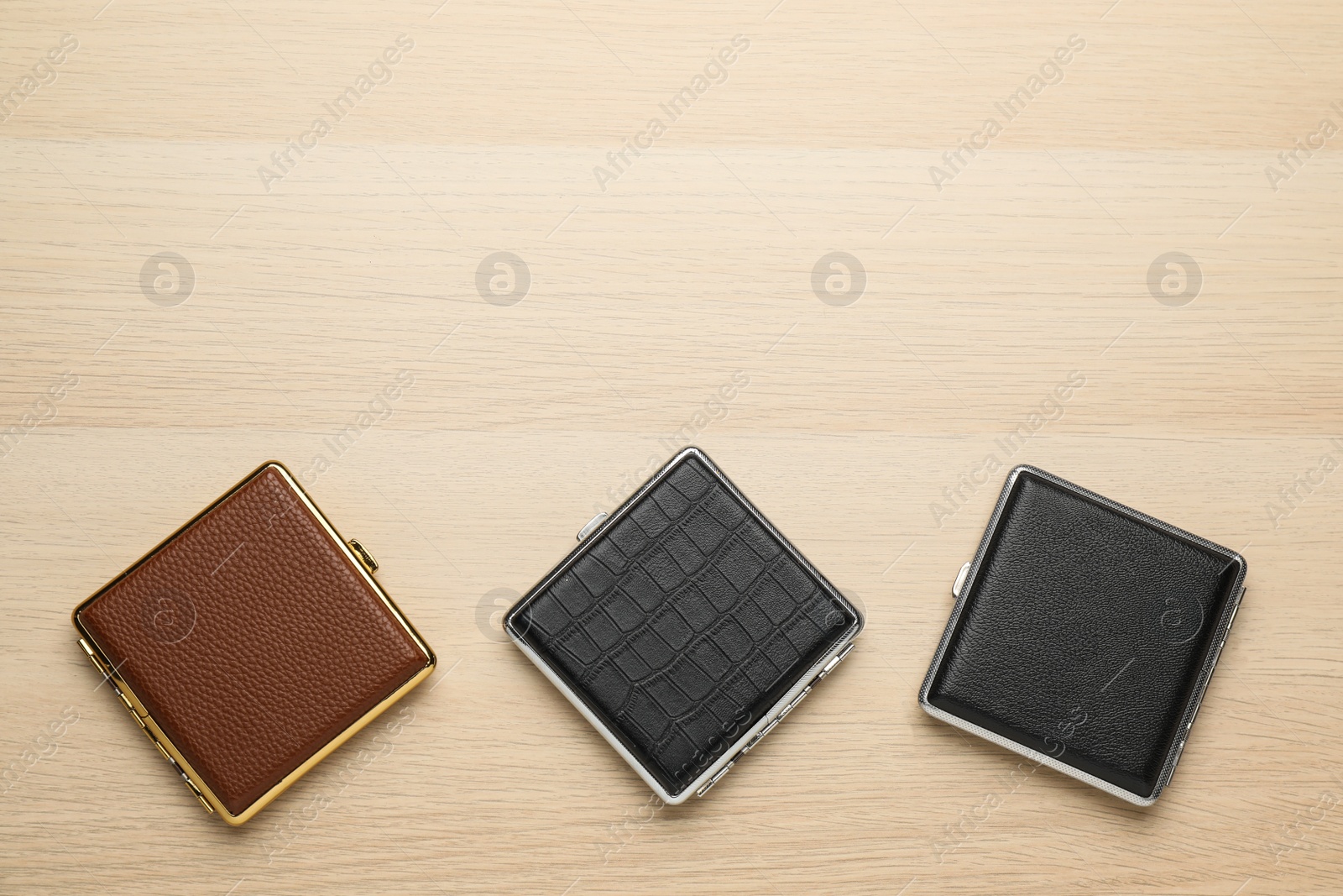 Photo of Closed leather cigarette cases on wooden table, flat lay. Space for text