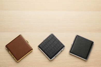 Photo of Closed leather cigarette cases on wooden table, flat lay. Space for text