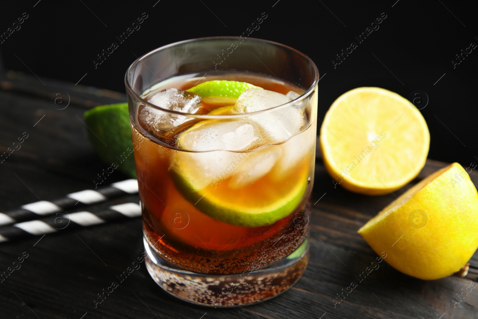 Photo of Glass of cocktail with cola, ice and cut lime on table against black background