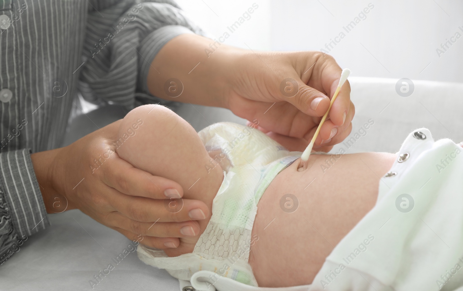 Photo of Mother cleaning navel of her baby with cotton bud on changing table, closeup