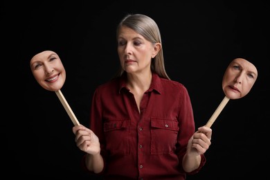 Image of Mature woman holding masks with his face showing different emotions on black background. Balanced personality