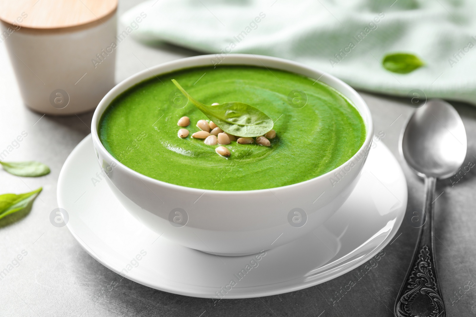 Photo of Bowl of healthy green soup with fresh spinach on grey table