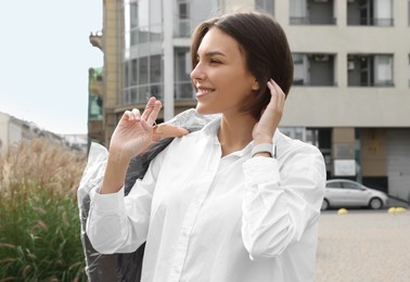 Photo of Woman holding garment cover with clothes outdoors. Dry-cleaning service