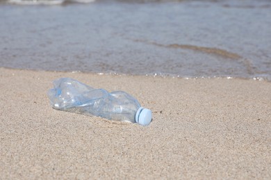 Photo of Used plastic bottle on sand near water. Recycling problem