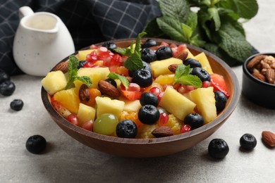 Delicious fruit salad in bowl, berries, nuts and fresh mint on grey table