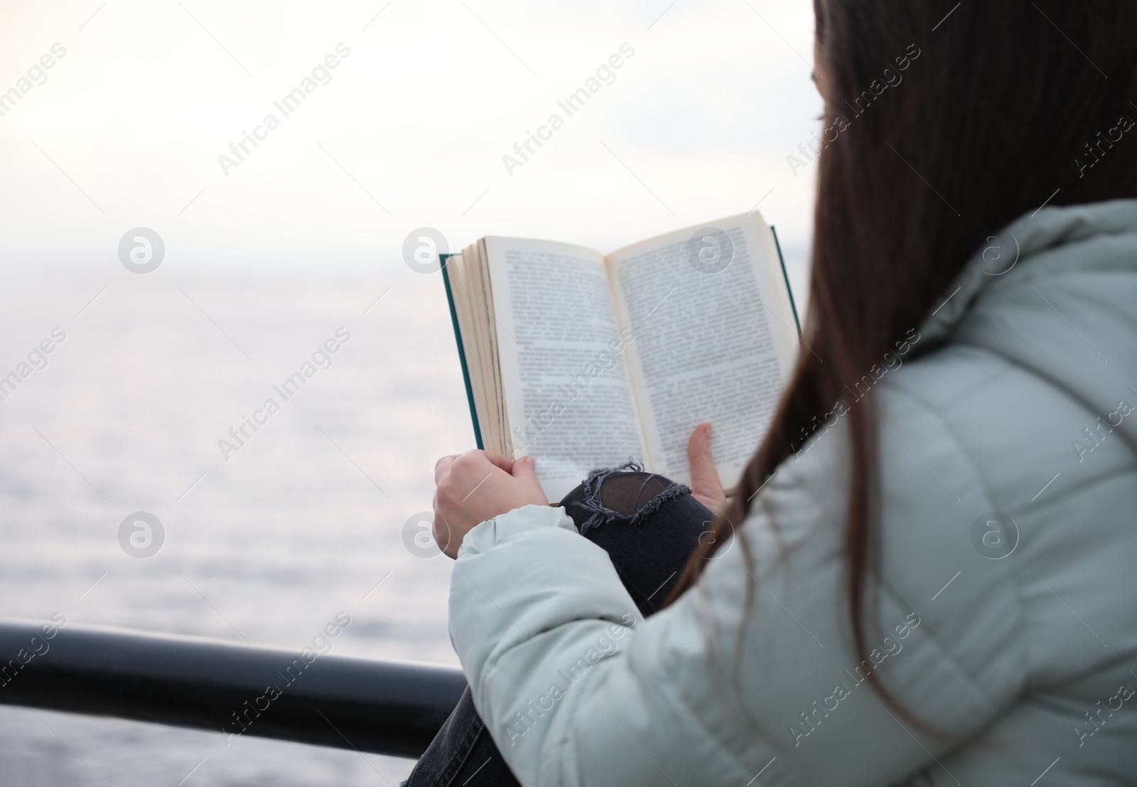 Photo of Woman reading book near river on cloudy day