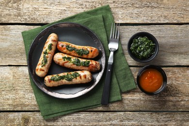 Photo of Tasty fresh grilled sausages served with sauces on wooden table, flat lay