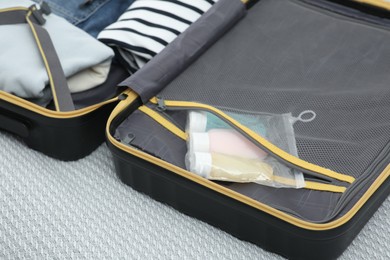 Photo of Plastic bag of cosmetic travel kit in suitcase on bed. Bath accessories