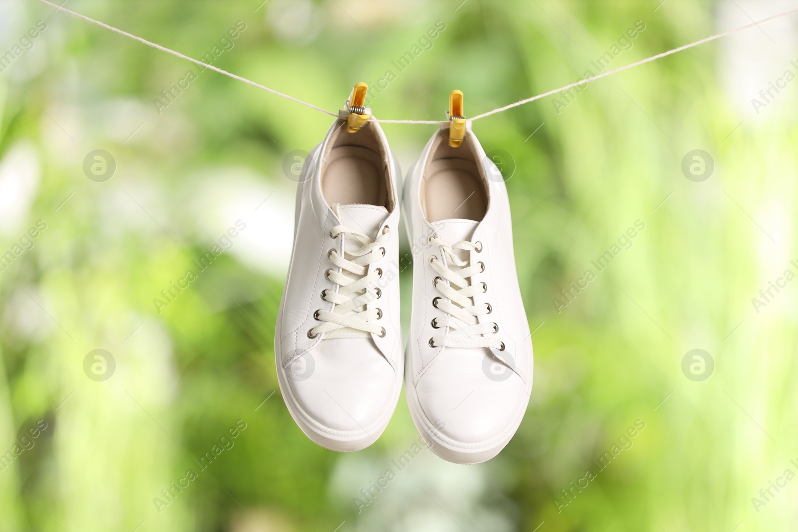 Photo of Stylish sneakers drying on washing line against blurred background